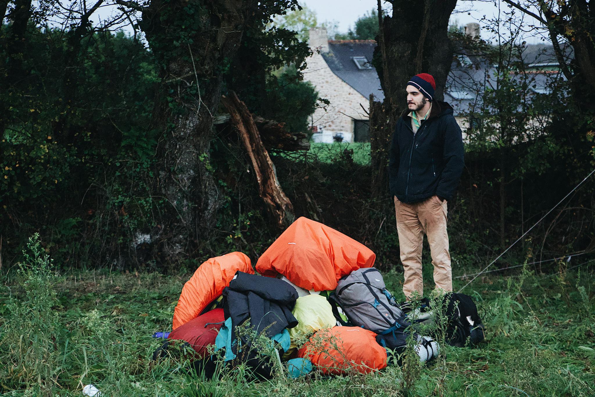Adult man standing by camping gear in a lush forest setting. Perfect for outdoor adventure themes.