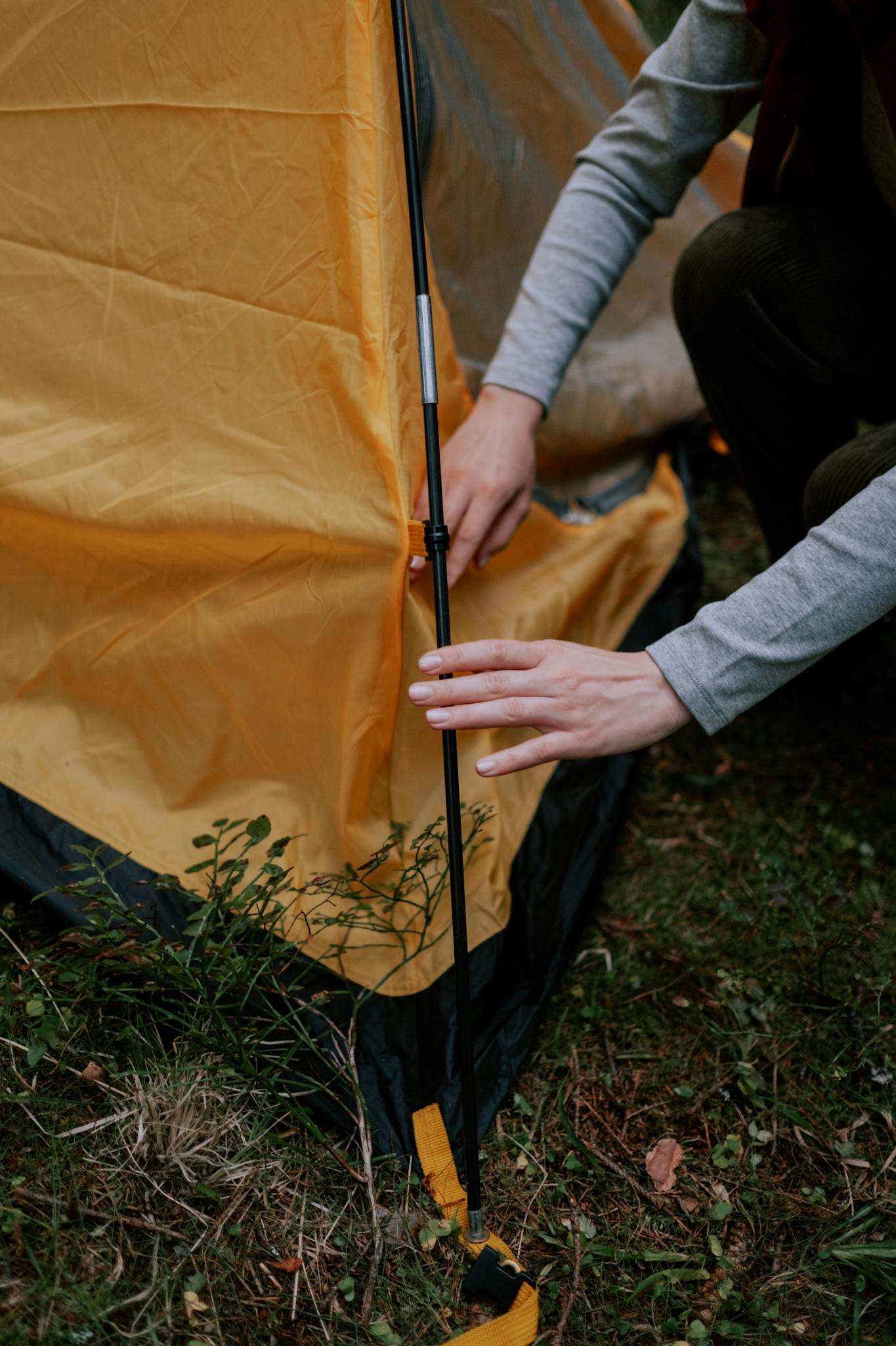 Close-up of a person setting up a tent, focusing on hands and tent pole assembly.