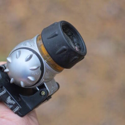 Hand holding plastic gray black headlamp outdoors on brown background