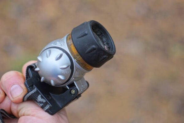 Hand holding plastic gray black headlamp outdoors on brown background
