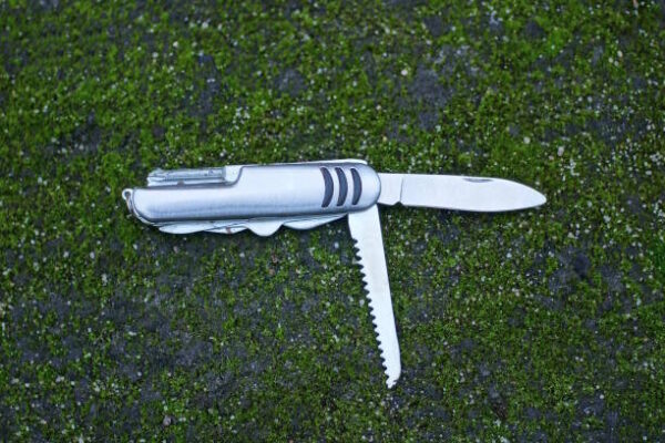 One old gray iron open folding multitool knife lies on green moss on the street