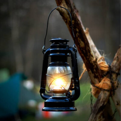 Close up of illuminated lantern hanging from wood at campsite